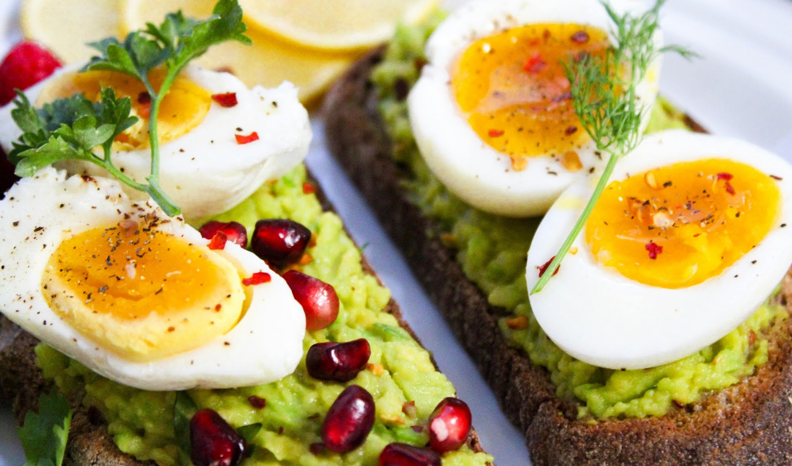 A close-up of avocado toast topped with soft-boiled eggs, pomegranate seeds, and fresh herbs, served on whole-grain bread with a side of lemon slices. Aside from supporting prostate health, nutritious foods can help prevent digestive and kidney diseases.